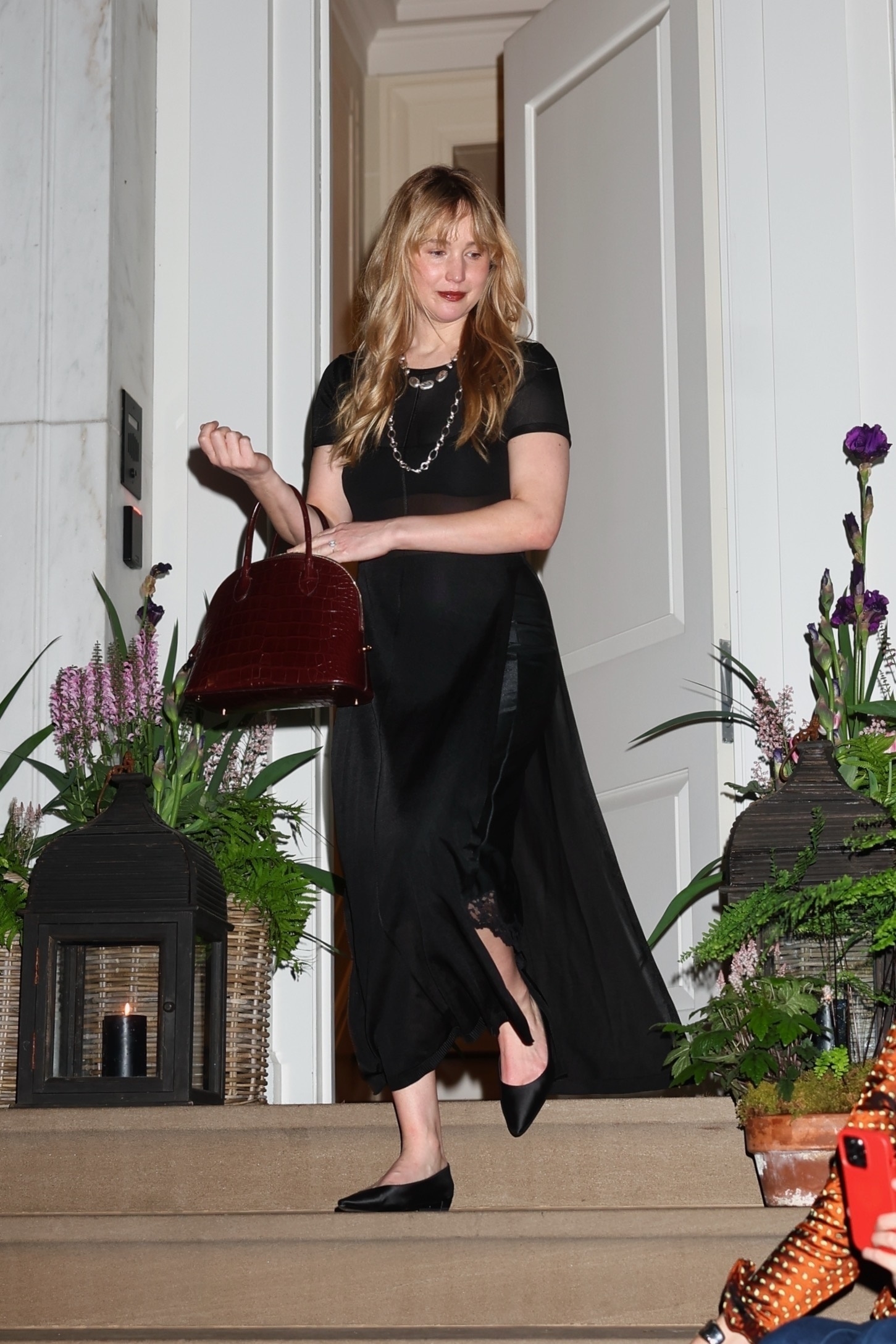 Actress Jennifer Lawrence attends an exclusive fashion event at the house of Lauren Santo Domingo, now owned by Ralph Lauren, in New York, looking chic in a black midi dress, burgundy handbag, and black pointed flats.