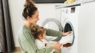 Woman loading a washer dryer combo with her baby on her lap.