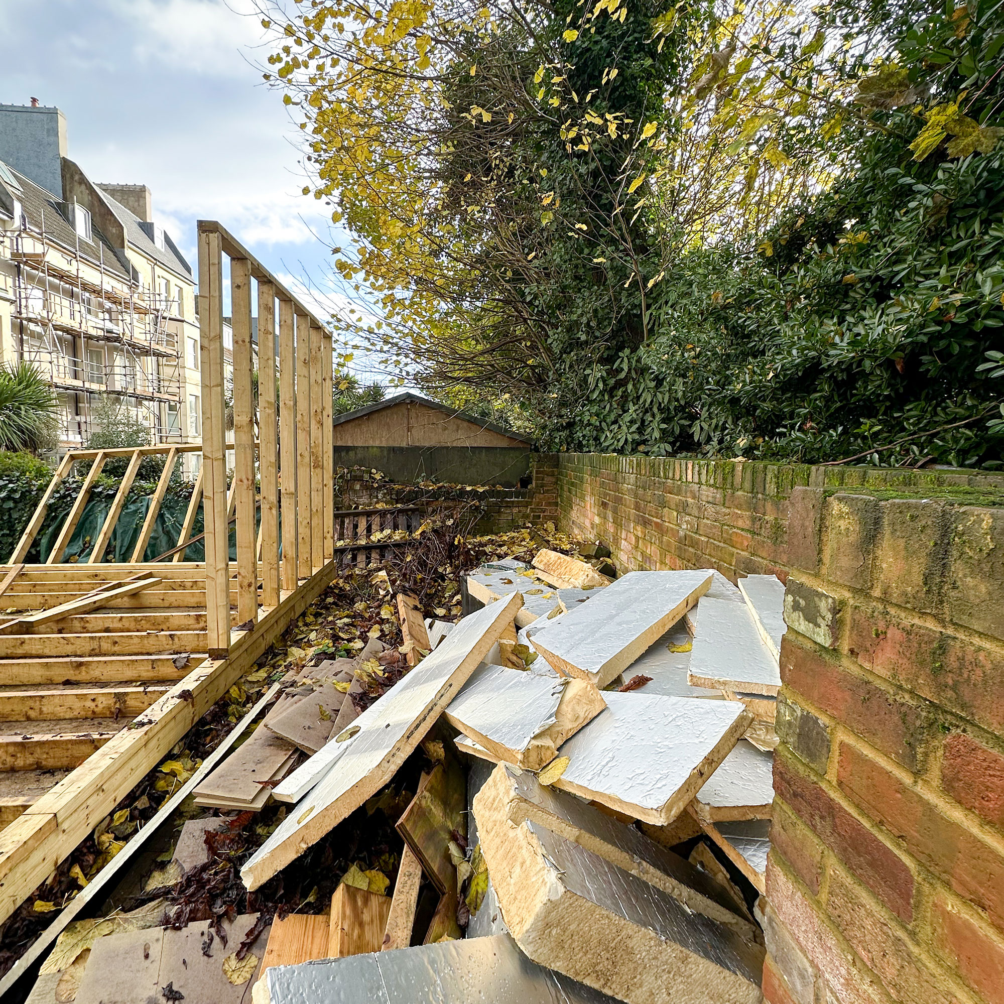 Pile of rubble between garden wall and wooden structure of summerhouse being erected