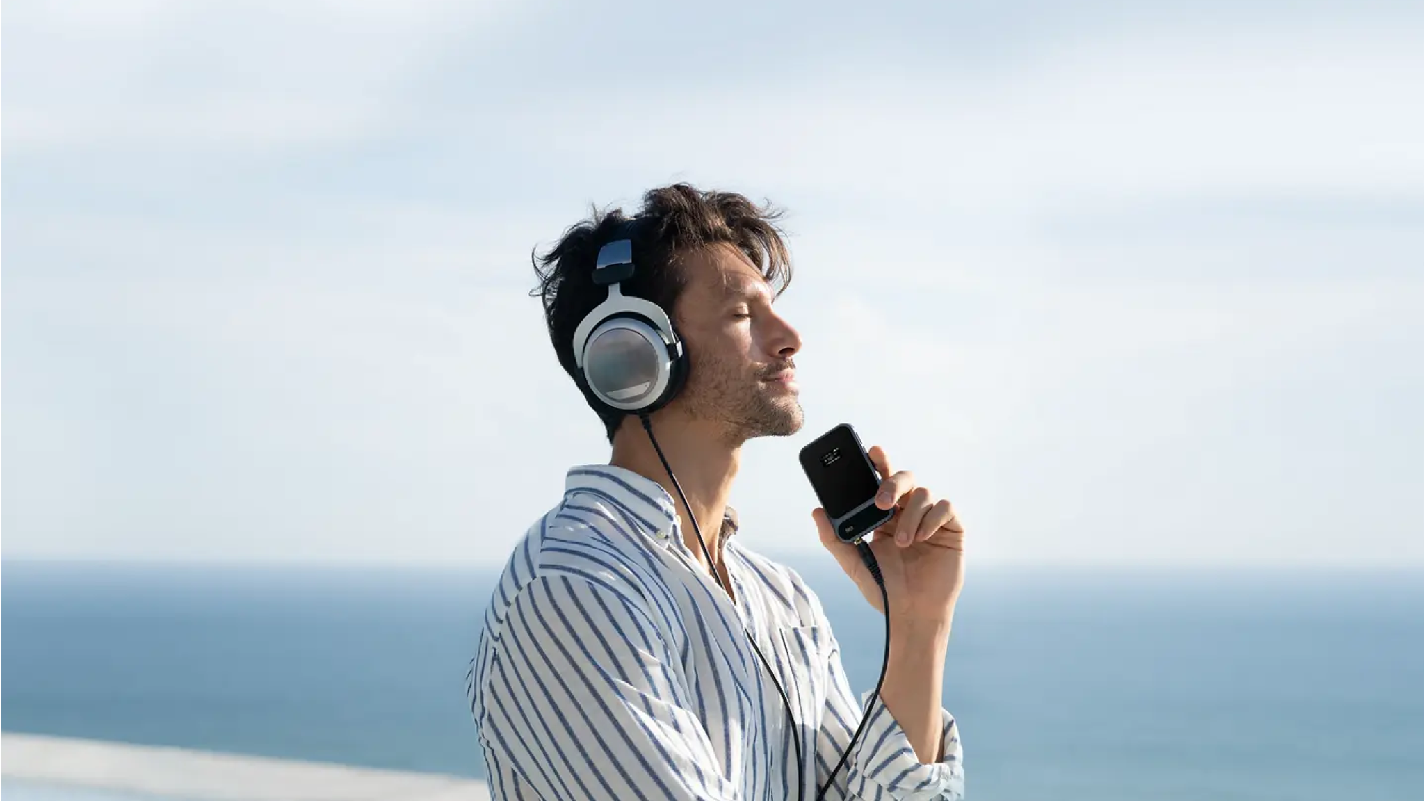 A man wearing big headphones connected to the Khadas Tea Pro in front of a seascape