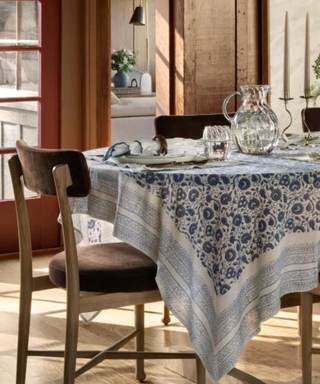A dining room with a blue and white tablecloth and wooden chairs.