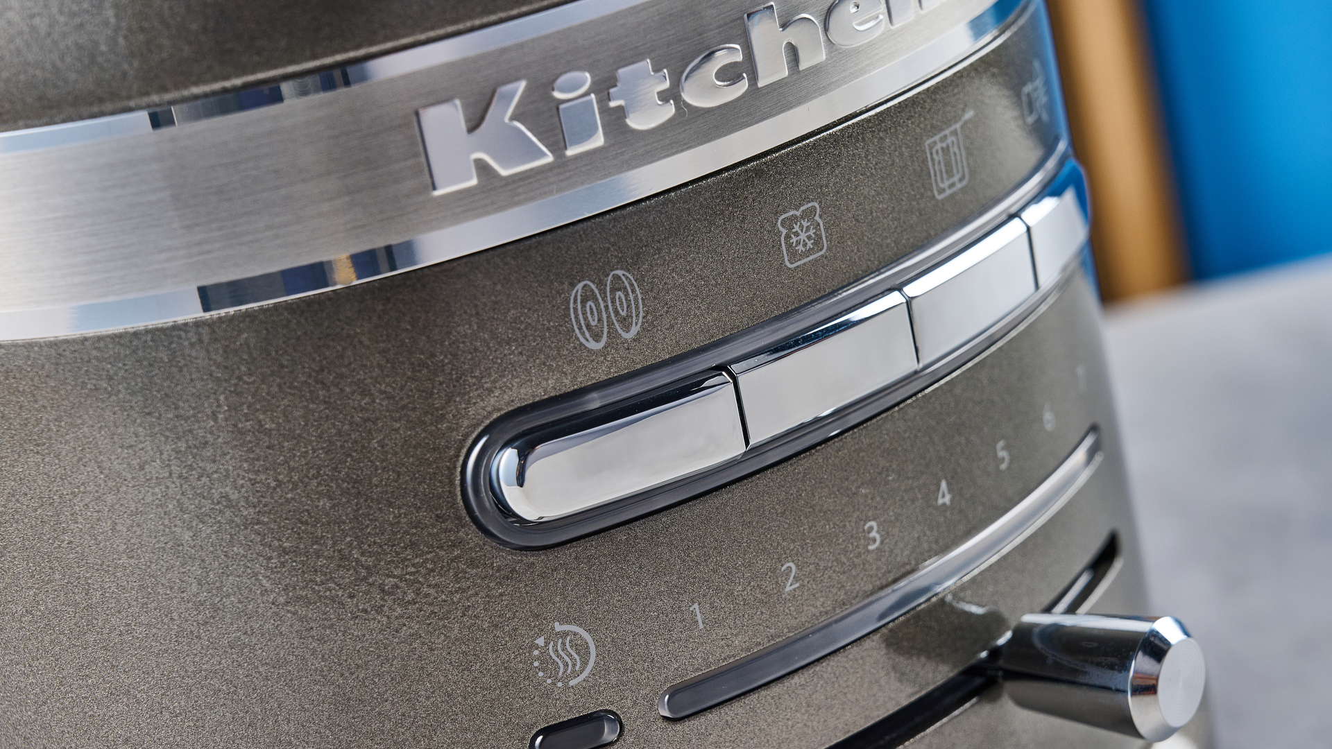 A photograph of the KitchenAid Pro Line toaster on a stone work surface with a blue and wooden background