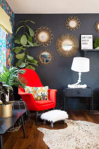 a living room with orange chair, dark navy walls and a collection of mirrors on the wall