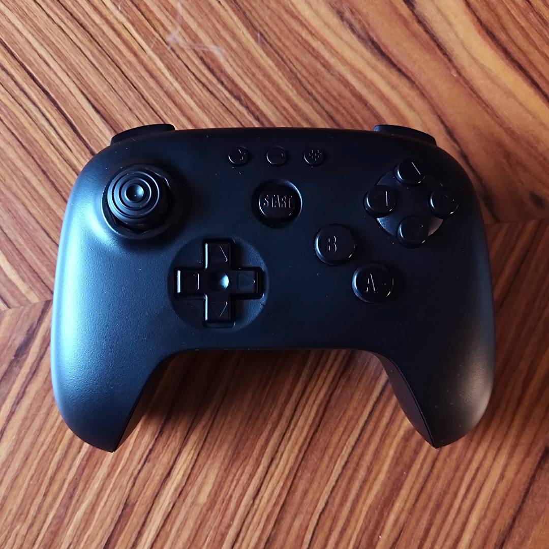8Bitdo Analogue 3D controller in black sitting on a woodgrain table.