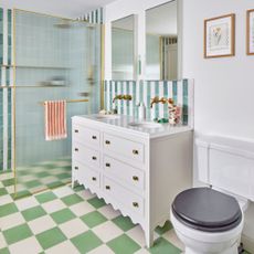 White painted bathroom with green and white checkerboard floor and blue and white tiles on the walls, with a white cabinet vanity in the middle