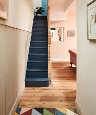 Pale pink painted hallway with dark blue painted stairs, light wooden flooring with geometric tiles