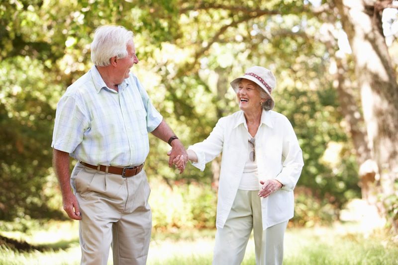 An older couple walks together, holding hands.