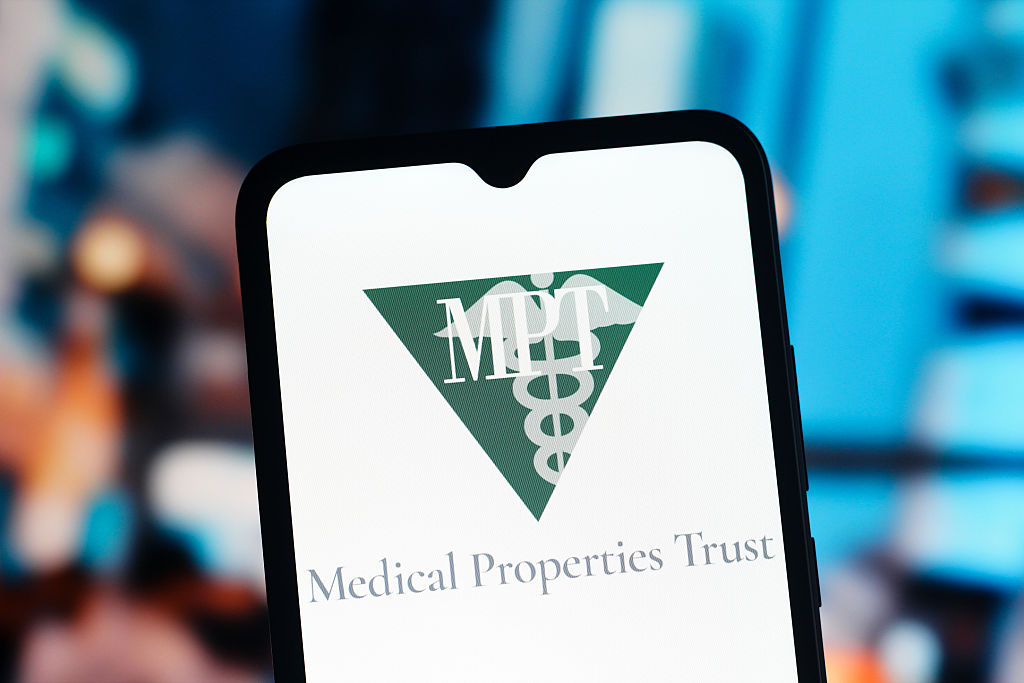 Medical Properties Trust logo on a smartphone with a blurred cityscape in the background