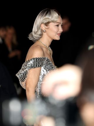 A photo of Gigi Hadid tucking the ends of her Hollywood waves behind her ears.