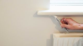 man painting underside of window sill with paint brush