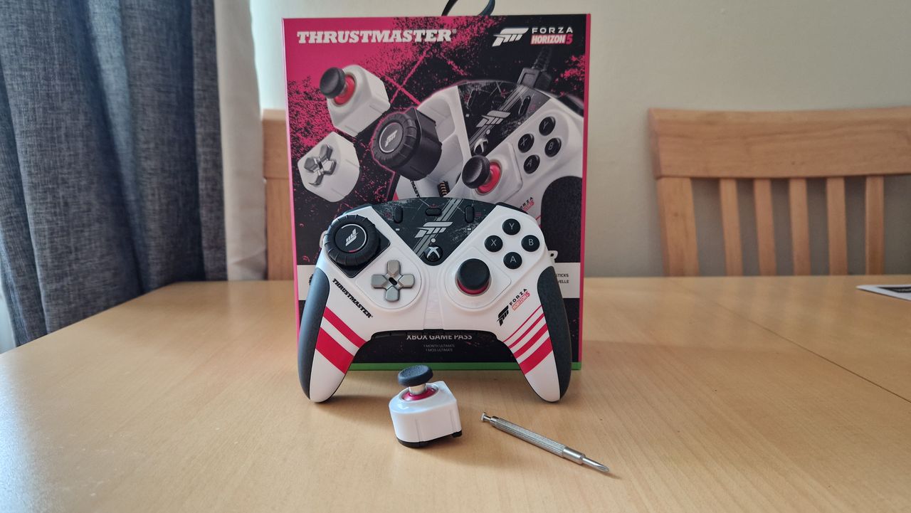 Thrustmaster eSwap XR Pro Controller pictured in front of its box on a wooden table, with a spare swappable module and multi-tool sitting in front of it