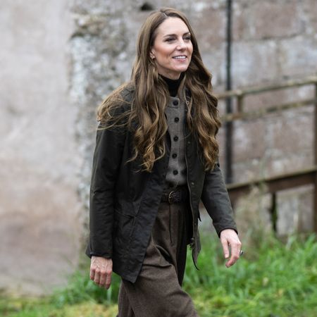  Princess Kate wearing a fall jacket walking in front of a stone building 