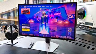 Samsung Odyssey OLED G6 with Fortnite main menu on screen sitting on desk next to window