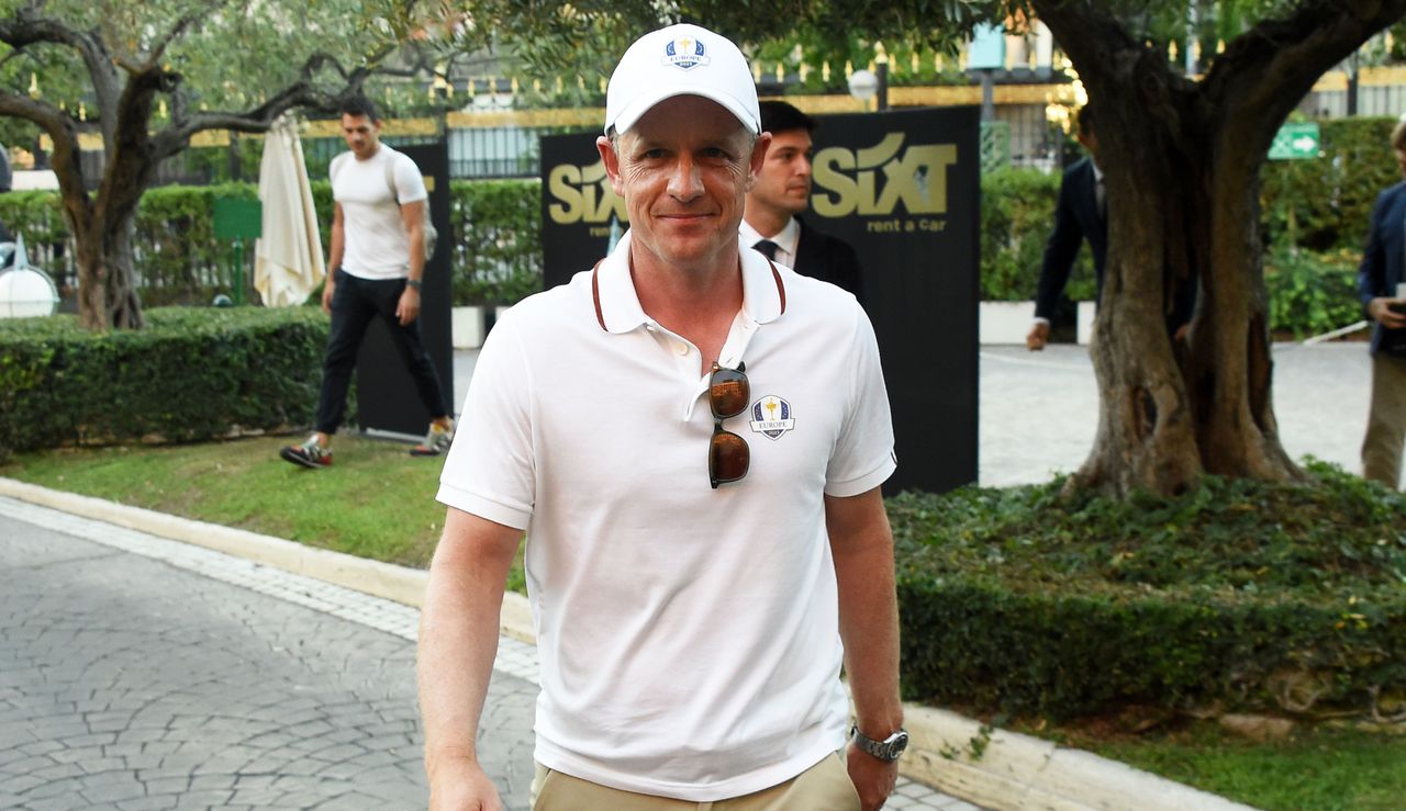 Luke Donald smiles at the camera as he walks along a path