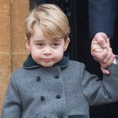 Prince George as a toddler wearing a gray coat holding his dad's hand