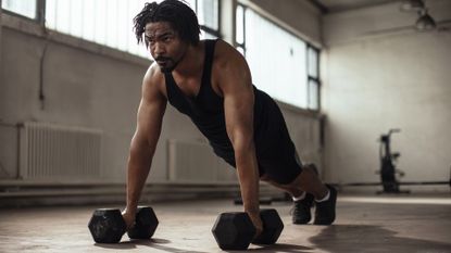 Young fit African American man doing pushups with dumbbells in the gym
