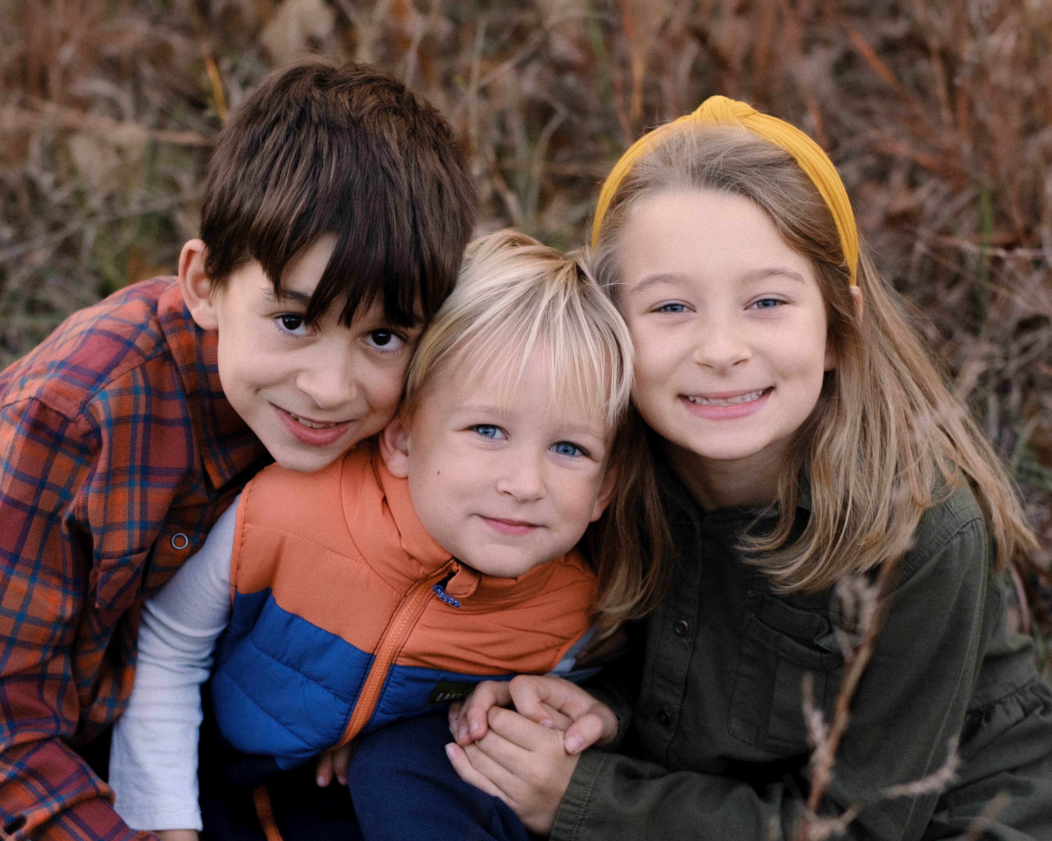 A photo of three children in a field of brown grass