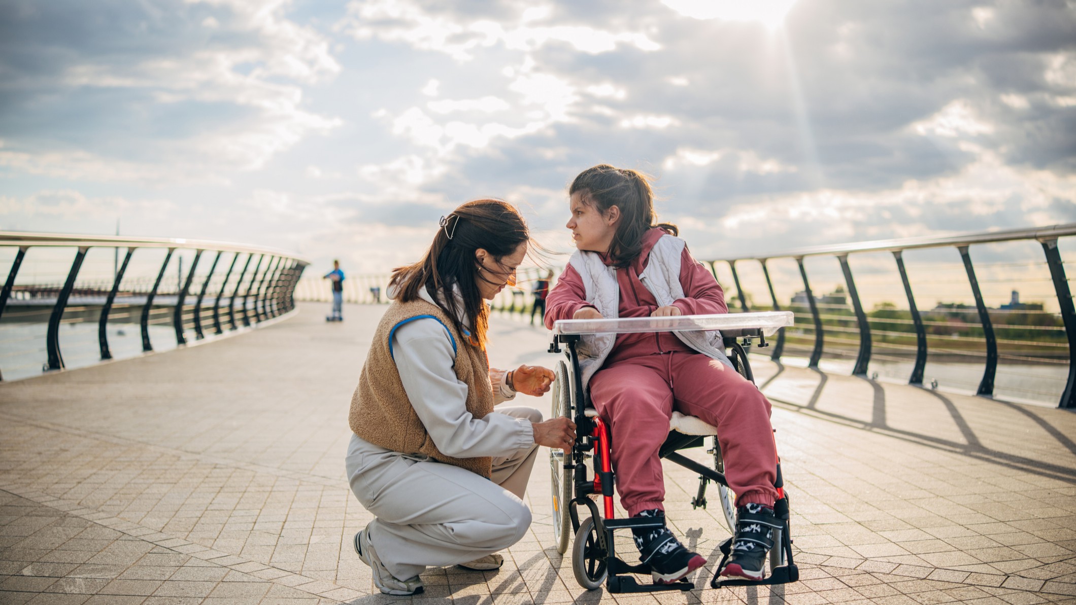 A woman kneels to fix something on a child's wheelchair. 