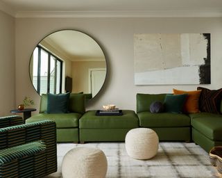 neutral living room with dark green sofa and round wall mirror