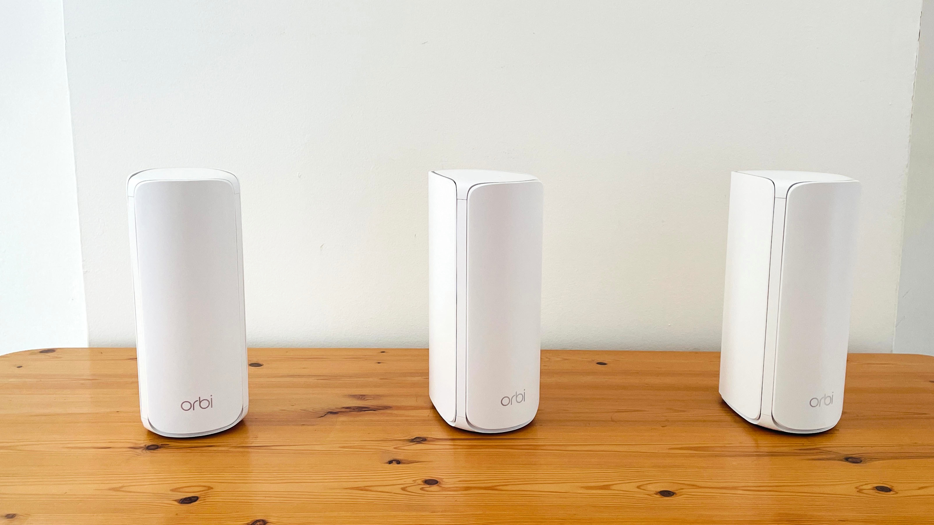 Enrutadores Netgear Orbi 770 en fila apoyados sobre la mesa