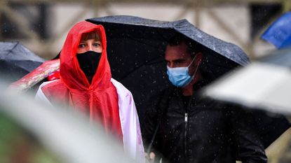 People wearing face masks shelter from the rain.