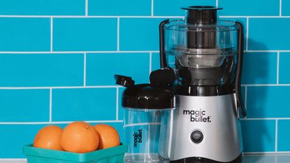 Magic Bullet Mini Juicer with citrus fruit in basket, with blue wall tiled background