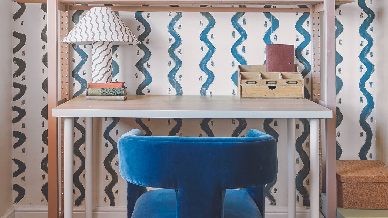 Home office with rickrack wallpaper, desk and blue armchair.