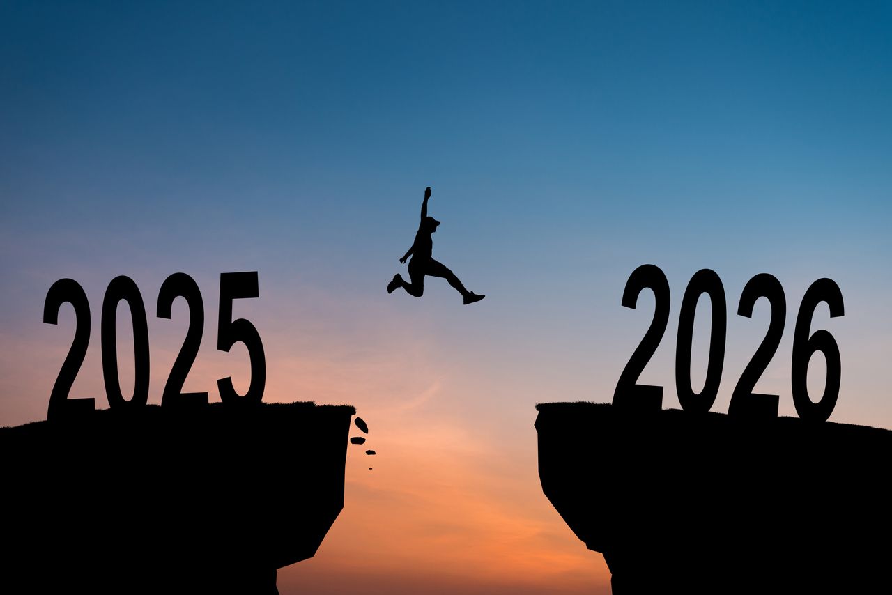 Silhouette of a person jumping over a cliff from the year 2025 to the year 2026, with a sunset in the background.