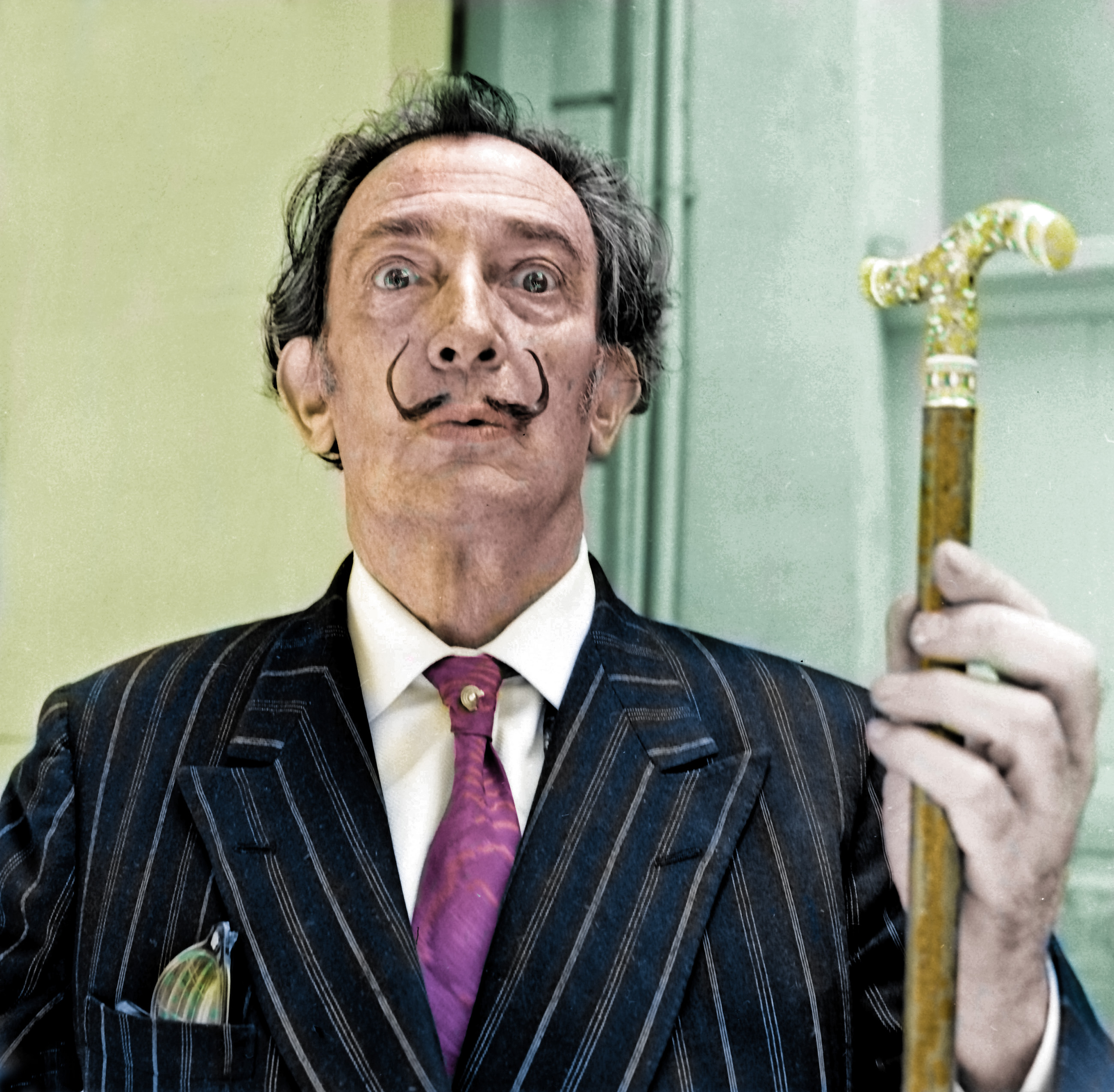 A man in a thin moustache holds up a gold cane