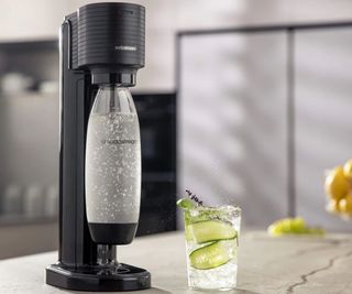 SodaStream Gaia on a countertop with a glass of sparkling water infused with cucumber