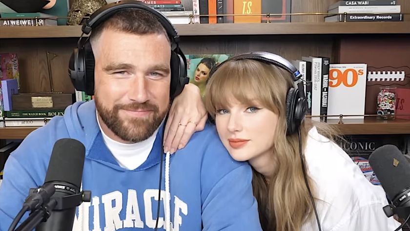 Taylor Swift leaning on Travis Kelce while they both wear headphones on the New Heights podcast. 