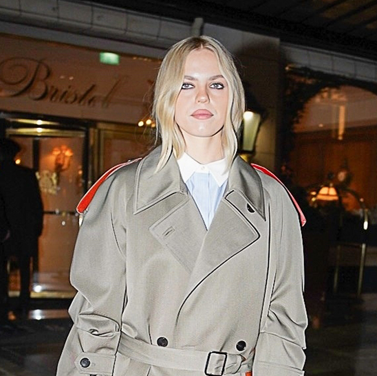 Renee Rapp wearing a Tory Burch trench, striped button-down shirt, and red heels