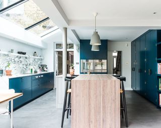 An example of side return extension ideas showing a wooden island in a kitchen with dark blue cabinets and a marble backsplash