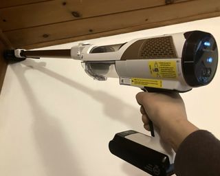 Paige Cerulli, a white woman, removing cobwebs from wooden ceiling using the handheld Shark Cordless Detect Pro Auto Empty vacuum cleaner