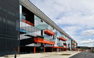The facade of the Here East complex is all glass, with bright orange balconies.