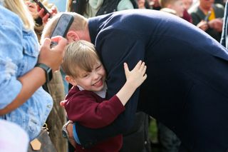 Prince William hugging a little boy in a maroon sweatshirt at a March 2025 soccer event