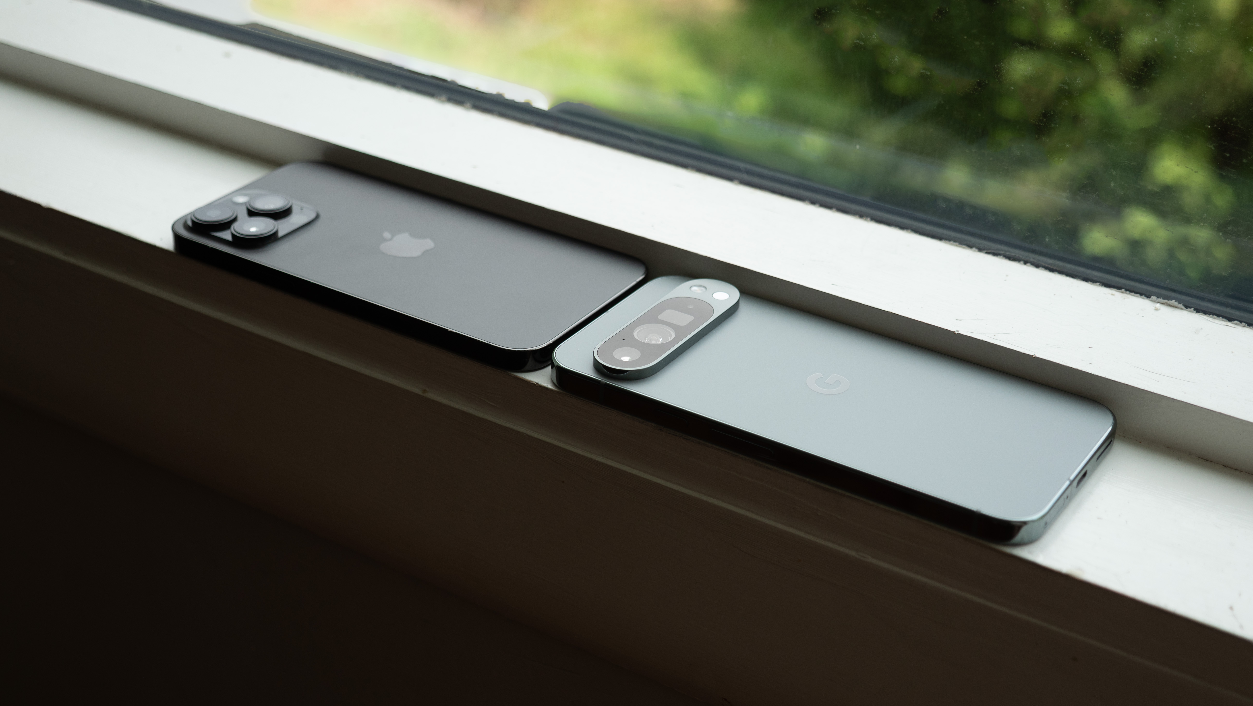 An Apple iPhone 14 Pro Max next to a Google Pixel 9 Pro XL on a windowsill