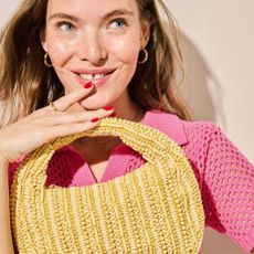 Young woman dressed in pink crotchet top holding woven holiday bag