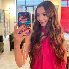 Dionne Brighton in a pink dress, taking a mirror selfie to show the after result of the concave cut. Smiling, feeling very happy with the result.