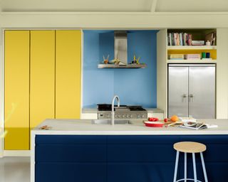 modern kitchen with dark blue island, light blue wall and bright yellow built-in cabinetry