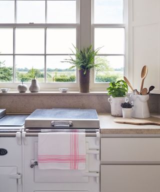 A white kitchen range cooker with silver hob cover and white fitted cupboards under a window.