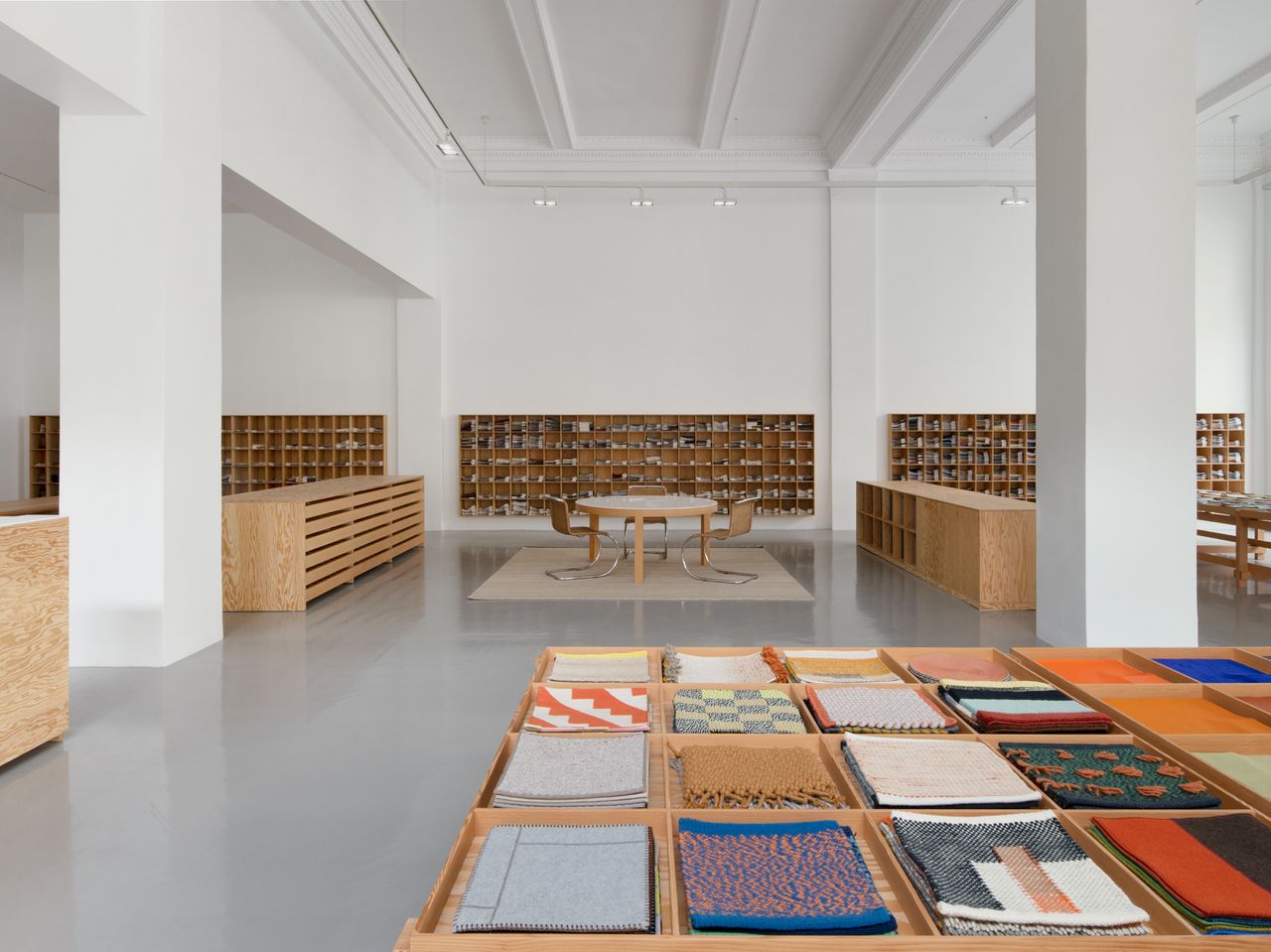 Colorful fabric samples are displayed in the foreground in custom wooden tables inside Maharam&#039;s new Gramercy showroom.