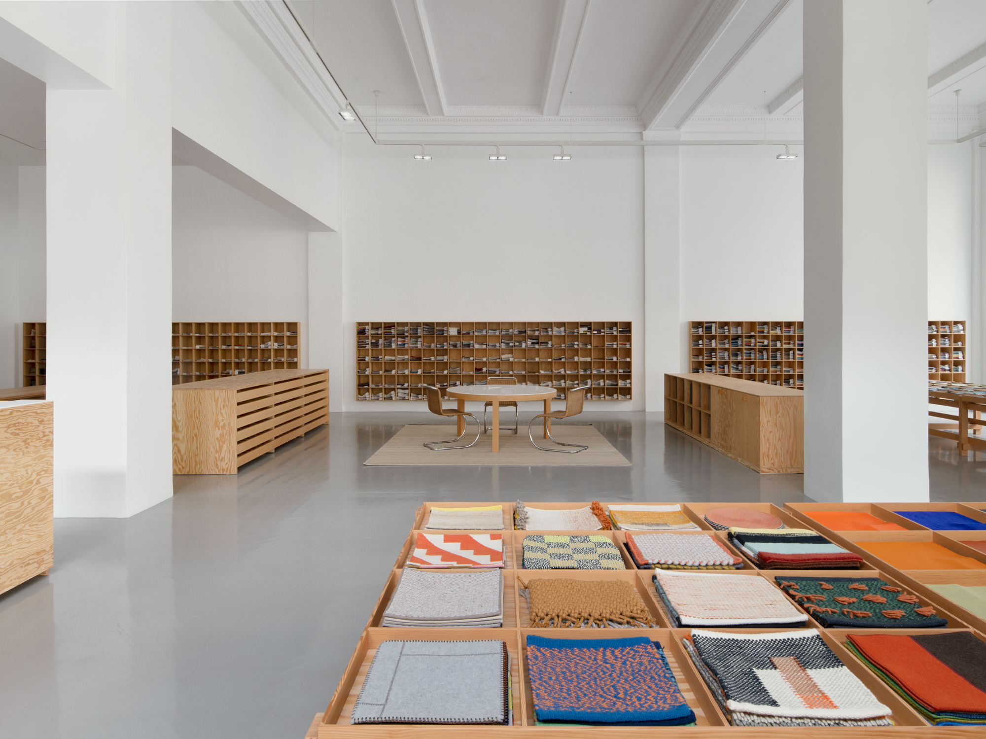 Colorful fabric samples are displayed in the foreground in custom wooden tables inside Maharam&#039;s new Gramercy showroom.