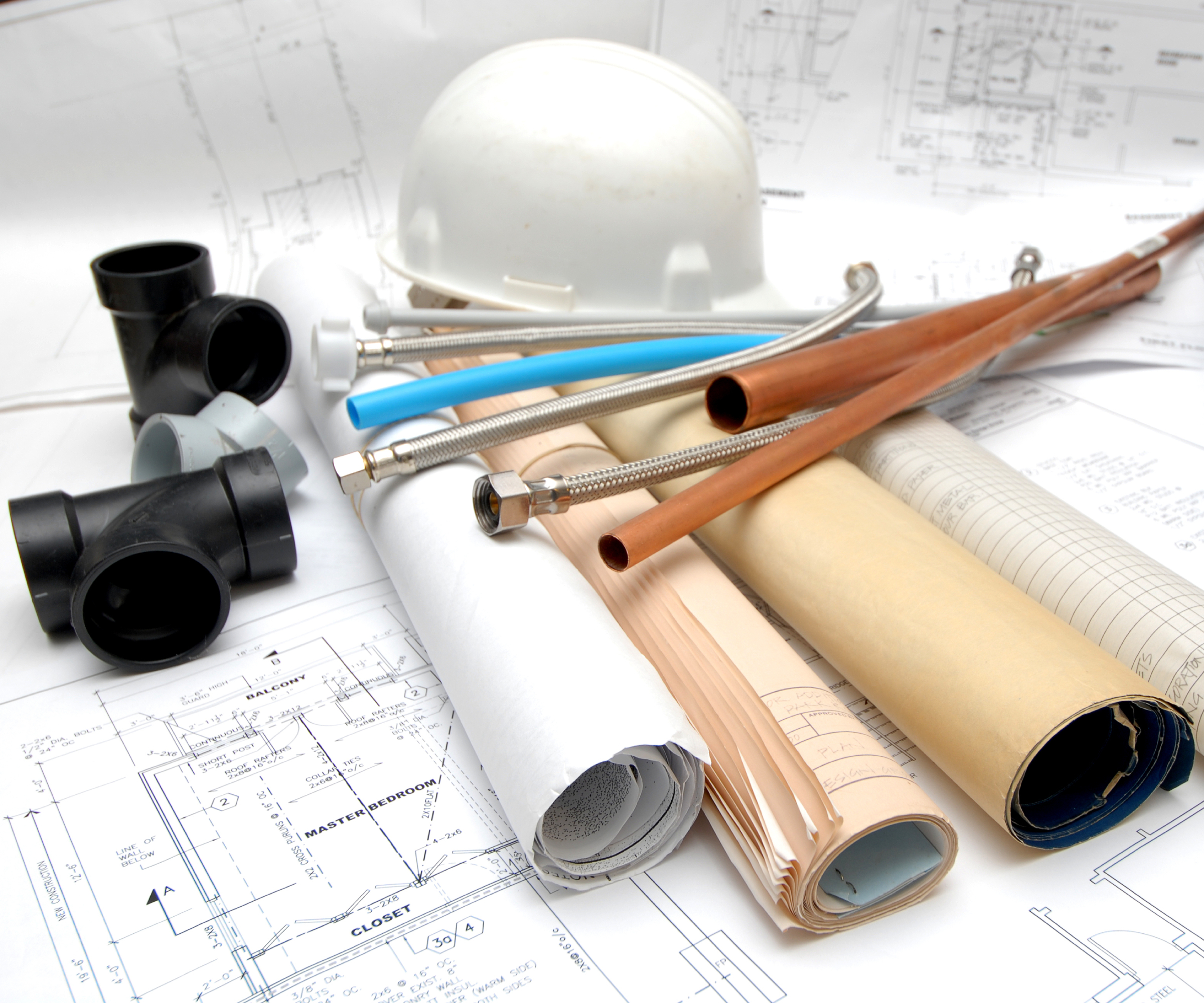 architect drawings with pipes, connectors and hard hat on top of them
