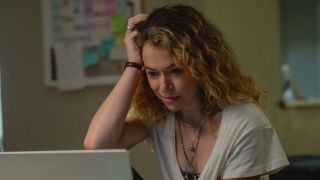 Tatiana Maslany looking down at a computer screen while resting her head on her hand.