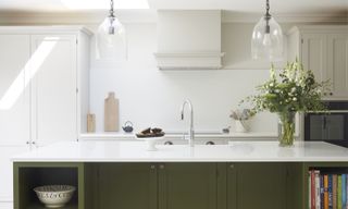 green and white kitchen with green painted kitchen island, white cabinetry, sink in kitchen island, glass pendants
