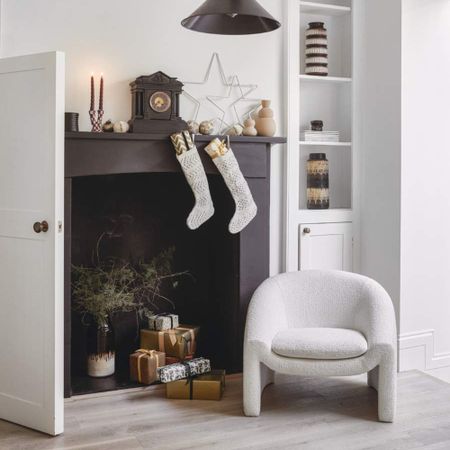 A corner of a living room in a monochrome colour scheme with a black fireplace decorated for Christmas with a white boucle chair next to it