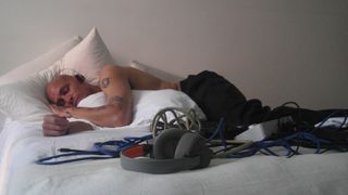 A producer wearing a pair of AIAIAI Tracks lying on a bed next to a pair of TMA-2 Wireless headphones