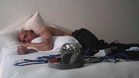 A producer wearing a pair of AIAIAI Tracks lying on a bed next to a pair of TMA-2 Wireless headphones