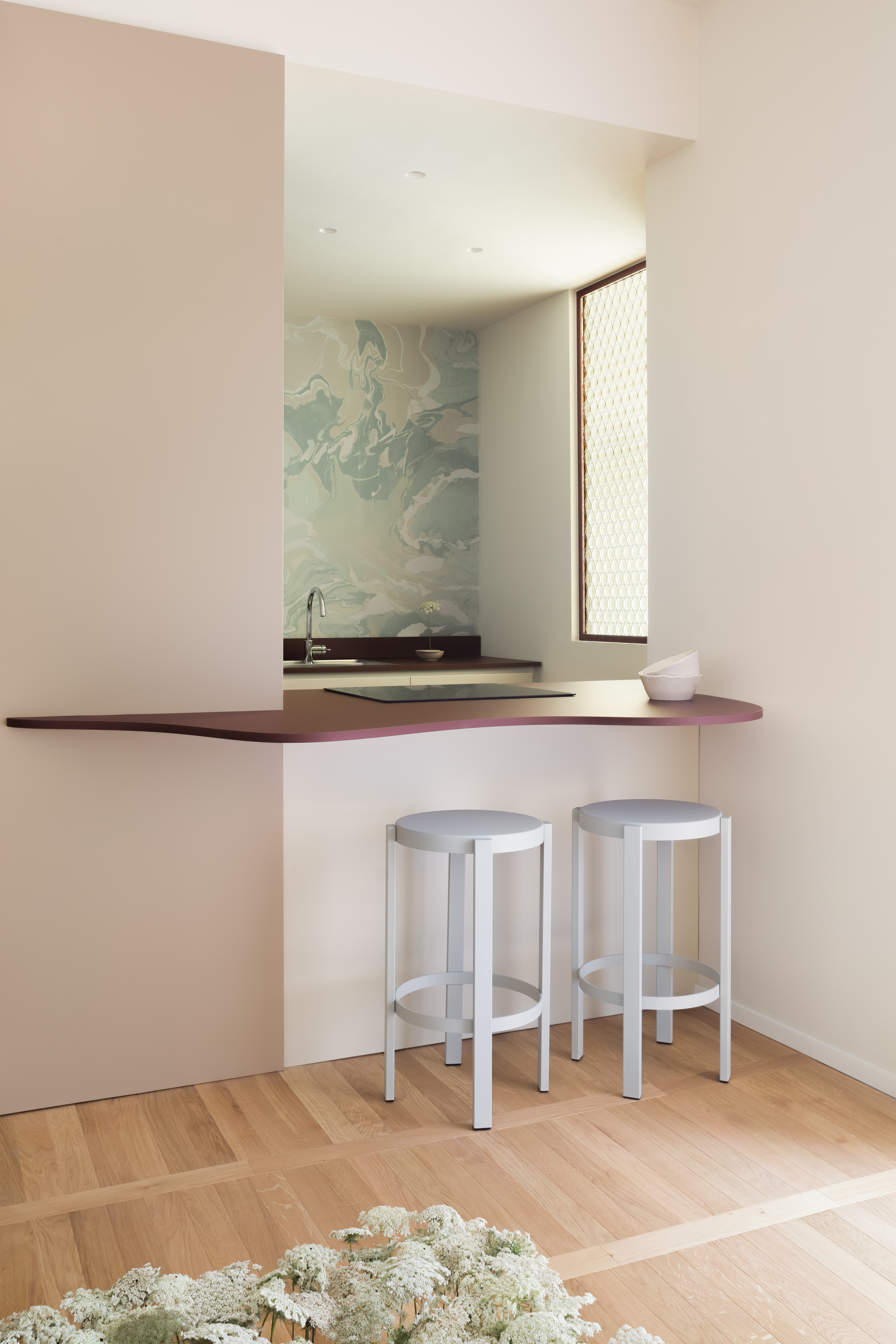 A kitchen with a hatch island in a curving shape and two white stools beside it